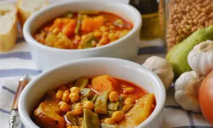 Dos cuencos de olla gitana murciana, un guiso tradicional con garbanzos, calabaza y judías verdes. Acompañado de pan y ingredientes frescos.