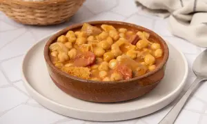 Un plato humeante de callos con garbanzos, chorizo y trozos de carne, servido en una cazuela de barro.