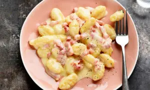 Ñoquis a la carbonara cremosos y deliciosos, cubiertos con trozos de panceta y pimienta negra, servidos en un plato rosa.