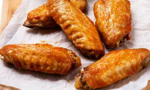 Cinco alitas de pollo al horno crujientes, cubiertas con una salsa brillante y apetitosa, listas para disfrutar.