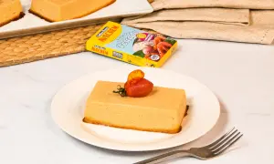 Pastel de merluza servido en plato blanco, decorado con tomate y hierbas. Caja de caldo de pescado Avecrem al fondo.