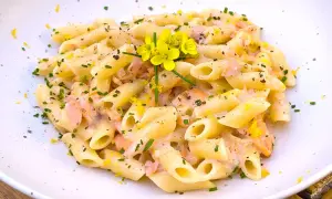 Pasta penne cremosa con trozos de salmón rosado, ralladura de limón y flores amarillas. Un plato delicioso.