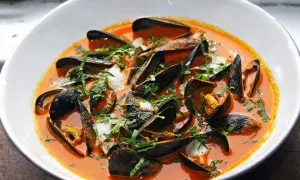Un tazón blanco rebosante de mejillones al vapor en una salsa roja vibrante, adornado con hierbas frescas picadas.