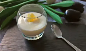 Delicioso postre de lemon curd en copa, decorado con un trozo de limón. Una cuchara plateada y tulipanes negros completan la escena.