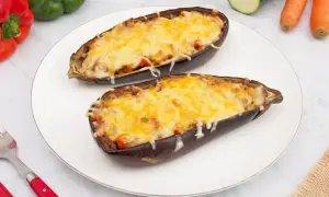 Dos mitades de berenjenas rellenas de verduras y cubiertas de queso gratinado, listas para disfrutar.