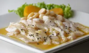 Delicioso tiradito de corvina fresco, bañado en una salsa cítrica y adornado con semillas de sésamo negro, acompañado de camote y lechuga.