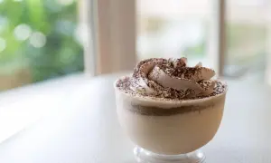 Delicioso mousse de café con crema batida y cacao espolvoreado, servido en un vaso transparente.