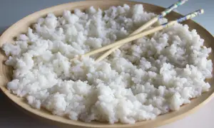 Arroz para sushi listo para preparar tus makis favoritos. Palillos cruzados sobre el arroz blanco y pegajoso en un cuenco de madera.
