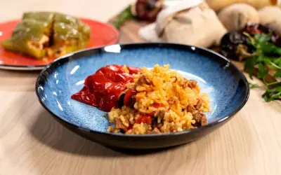 Plato azul con pimientos rellenos de arroz y carne. Otro pimiento verde relleno en un plato rojo al fondo.