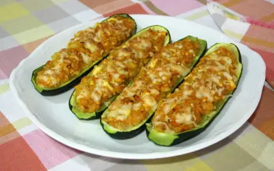 Cuatro calabacines rellenos de atún, gratinados con queso, servidos en un plato blanco sobre un mantel a cuadros.