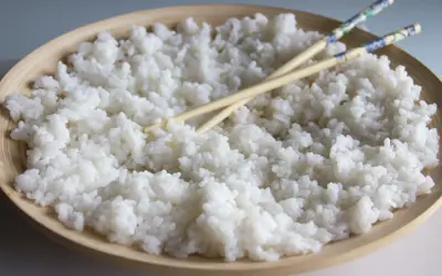 Arroz para sushi listo para preparar tus makis favoritos. Palillos cruzados sobre el arroz blanco y pegajoso en un cuenco de madera.