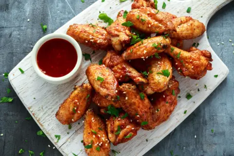 Deliciosas alitas de pollo fritas, doradas y crujientes, servidas con salsa y perejil picado.