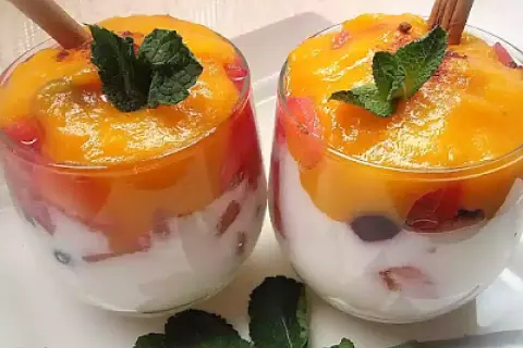 Dos copas de cristal con capas de yogur blanco, trozos de fruta roja y un delicioso mousse de mango coronado con menta y canela.