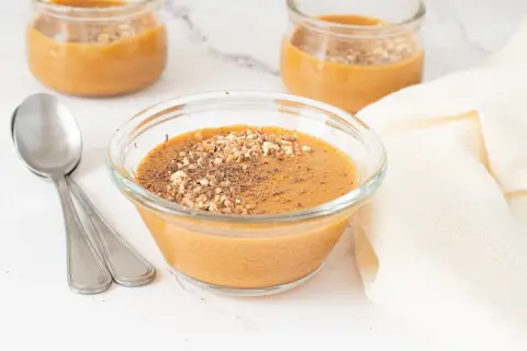 Delicioso postre cremoso, como baba de camelo, servido en un cuenco de cristal con nueces picadas y virutas de chocolate.