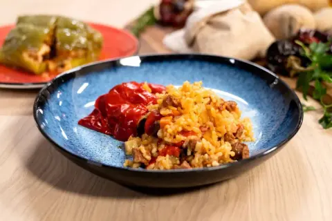 Plato azul con pimientos rellenos de arroz y carne. Otro pimiento verde relleno en un plato rojo al fondo.