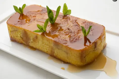 Pan de Calatrava, un postre dorado con caramelo líquido y hojas de menta, servido en una bandeja blanca.