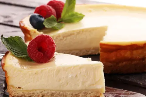 Deliciosa tarta de queso con galletas, coronada con frambuesas frescas y hojas de menta. Un trozo ya servido en un tenedor.