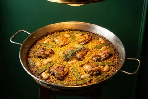 Paella valenciana recién hecha, con trozos de pollo dorado, judías verdes y garrofón, coronada con una ramita de romero.