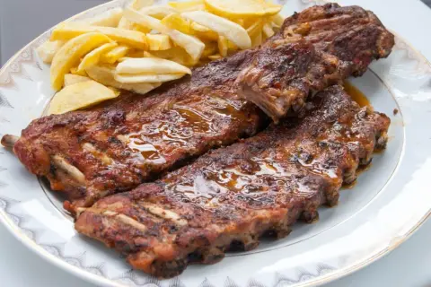 Costillas de cerdo jugosas y doradas, cubiertas de salsa brillante, acompañadas de papas fritas crujientes en un plato blanco.