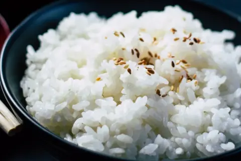 Un tazón de arroz blanco humeante, espolvoreado con semillas de sésamo, listo para ser disfrutado con palillos.