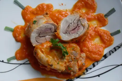 Contramuslos de pollo Thermomix enrollados con jamón, cubiertos de salsa de pimientos y decorados con perejil y cebolleta.