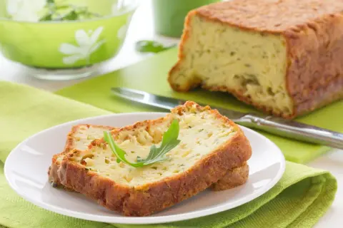 Rebanadas de un delicioso pastel de calabacín, esponjoso y dorado, servidas en un plato blanco con una hoja verde.