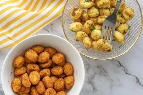 Dos boles llenos de ñoquis en freidora de aire, uno con especias y otro con perejil fresco. ¡Un aperitivo perfecto!
