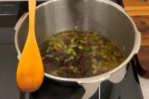 Olla express con alubias y verduras, lista para el tiempo de cocción. Una cuchara de madera descansa a un lado.