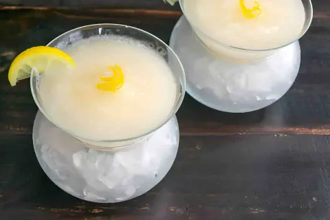 Dos copas de sorbete de limón, una con rodaja y otra con espiral de limón, servidas sobre hielo picado.