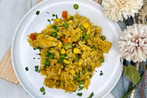 Arroz con pollo de la abuela, un plato casero con pollo tierno, guisantes, maíz y zanahoria, espolvoreado con perejil fresco.
