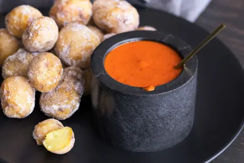 Papas arrugadas cubiertas de sal marina, listas para ser sumergidas en una salsa roja picante.