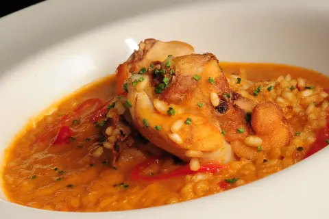 Delicioso arroz con conejo, trozos dorados de carne y pimientos rojos en una cremosa salsa, adornado con cebollino fresco.