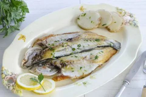 Lubina a la plancha, dorada y jugosa, servida con patatas y rodajas de limón. Un plato sencillo y delicioso.