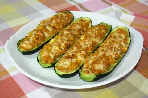 Cuatro calabacines rellenos de atún, gratinados con queso, servidos en un plato blanco sobre un mantel a cuadros.