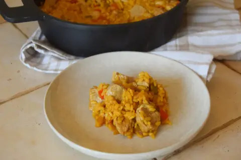 Un plato de arroz con carne, pimientos y trozos de cerdo, servido desde una paellera.