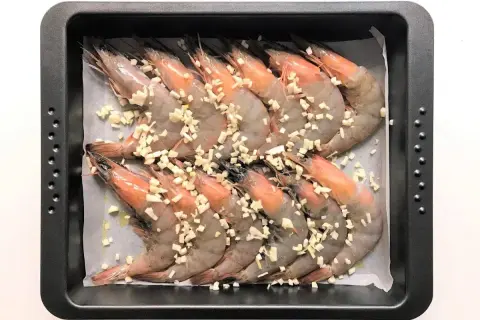 Langostinos al horno listos para cocinar, cubiertos con ajo picado en una bandeja.