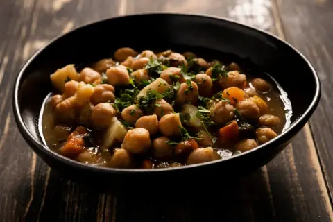 Un tazón de garbanzos con patatas y zanahoria, adornado con perejil fresco. Una deliciosa receta de garbanzos tradicional.