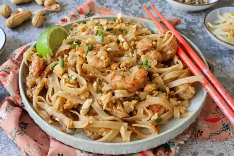 Un delicioso plato de pad thai con camarones, fideos de arroz, cacahuetes picados y cebollino.