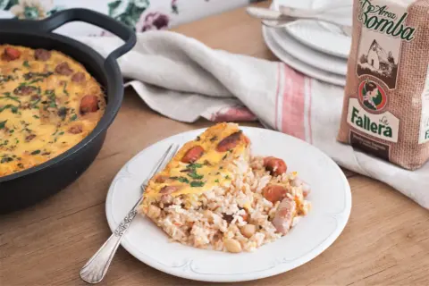 Un delicioso arroz con costra recién hecho, con trozos de salchicha y garbanzos, servido en un plato blanco.