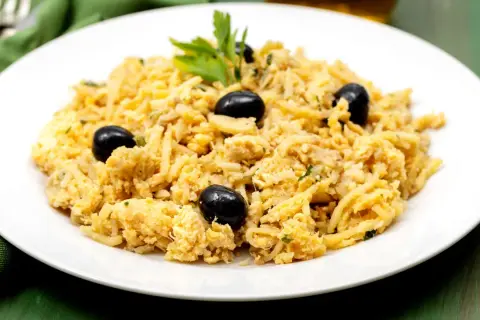 Delicioso bacalao a bras, un plato tradicional portugués con patatas finas, huevo y aceitunas negras, adornado con perejil fresco.