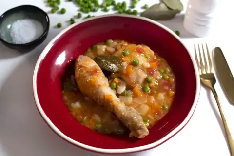 Un delicioso pollo a la jardinera en un cuenco rojo, con guisantes, zanahoria y laurel.