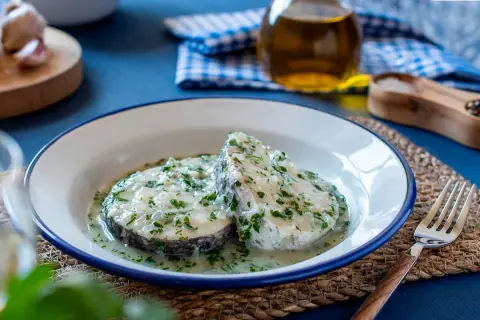Dos rodajas de merluza en salsa verde, con perejil picado y una cremosa salsa. Un plato casero listo para disfrutar.