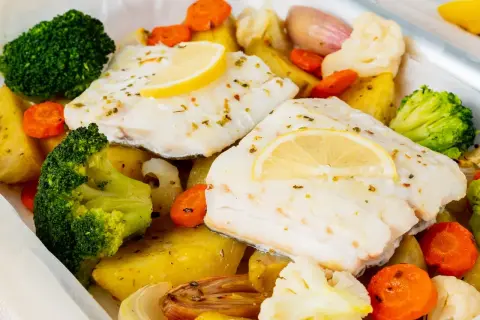 Bacalao al horno con patatas, brócoli, zanahorias y coliflor, todo asado en una bandeja.