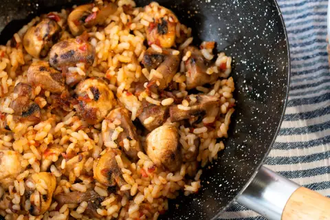 Arroz con champiñones recién hecho en sartén, con trozos dorados de champiñones y un toque de pimiento rojo.