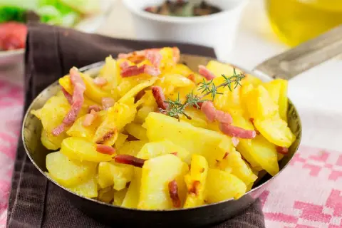 Patatas al microondas con trocitos de bacon crujiente y romero fresco, servidas en una sartén metálica. ¡Un plato sencillo y delicioso!