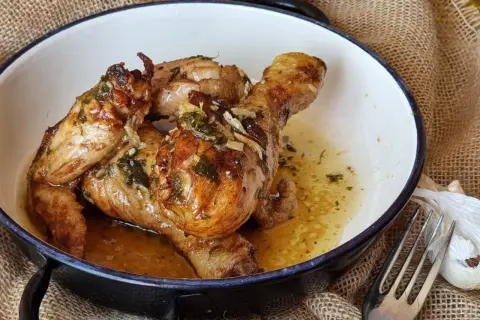 Sabroso pollo al ajillo dorado y jugoso, bañado en su propio jugo con ajo y hierbas, servido en una cazuela.