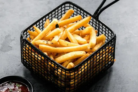 Cesta negra llena de crujientes patatas fritas doradas, listas para ser disfrutadas con una salsa roja.