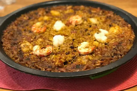 Arroz de tamboril con gambas y trozos blancos de pescado, servido en una paellera negra sobre una alfombrilla roja.