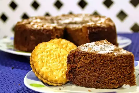 Un trozo de bizcocho de chocolate espolvoreado con azúcar glas junto a una galleta tipo Príncipe.
