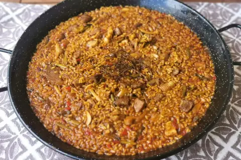 Arroz con secreto, un plato de paella con trozos de carne, pimientos y judías verdes, coronado con hierbas aromáticas.